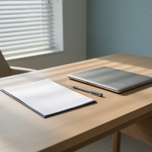 Bureau contemporain éclairé par une lumière douce, avec un dossier administratif vierge, des feuilles blanches, un stylo et un ordinateur fermé.